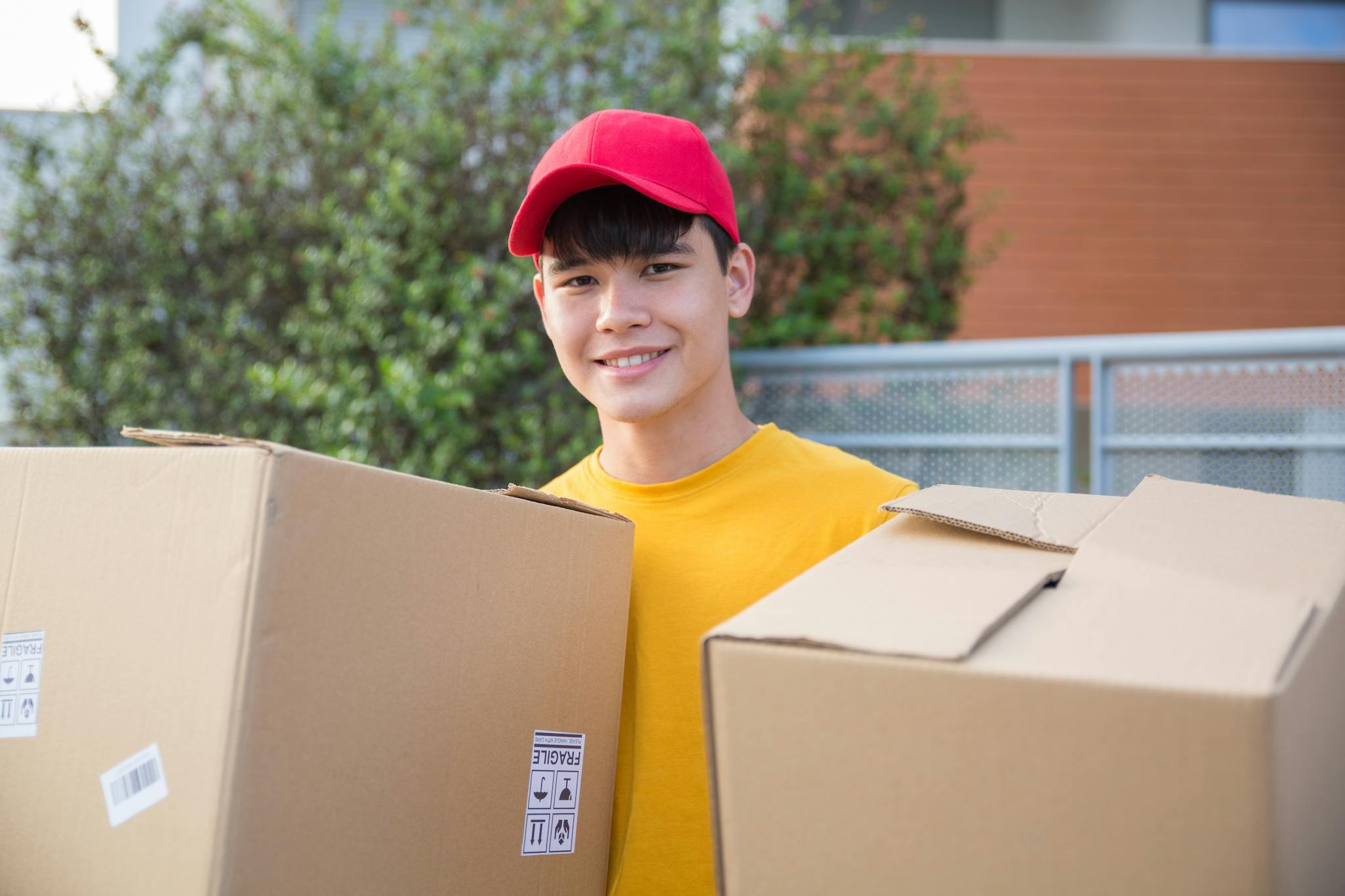 Smiling delivery man carrying boxes outside on a sunny day.